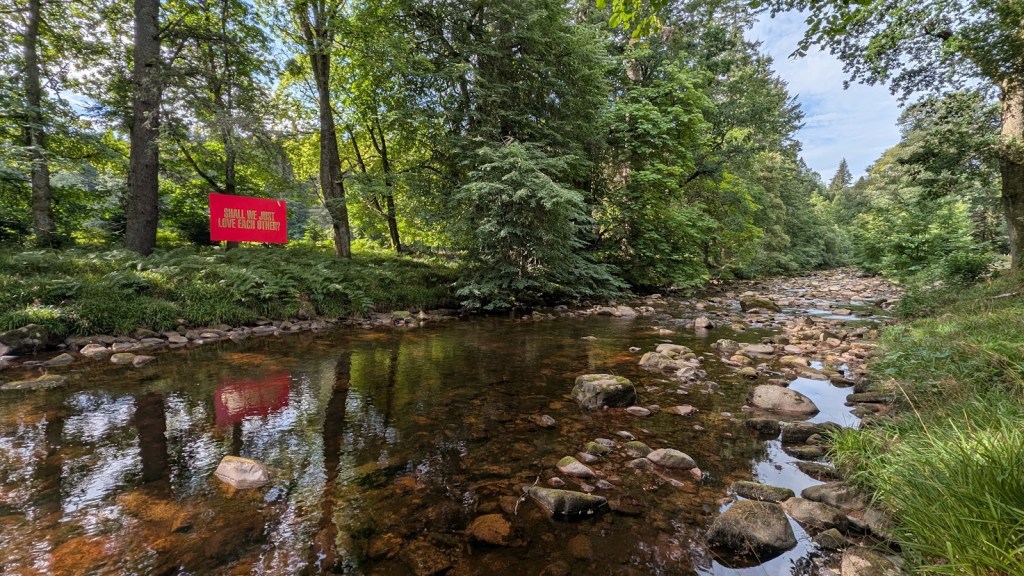 The Water of Dye and the sign in the river which reads, "Shall we just love each other"