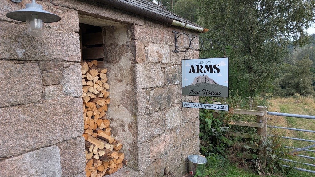 The Glen Dye Arms from the outside showing a stone building with the sign and a wood store.